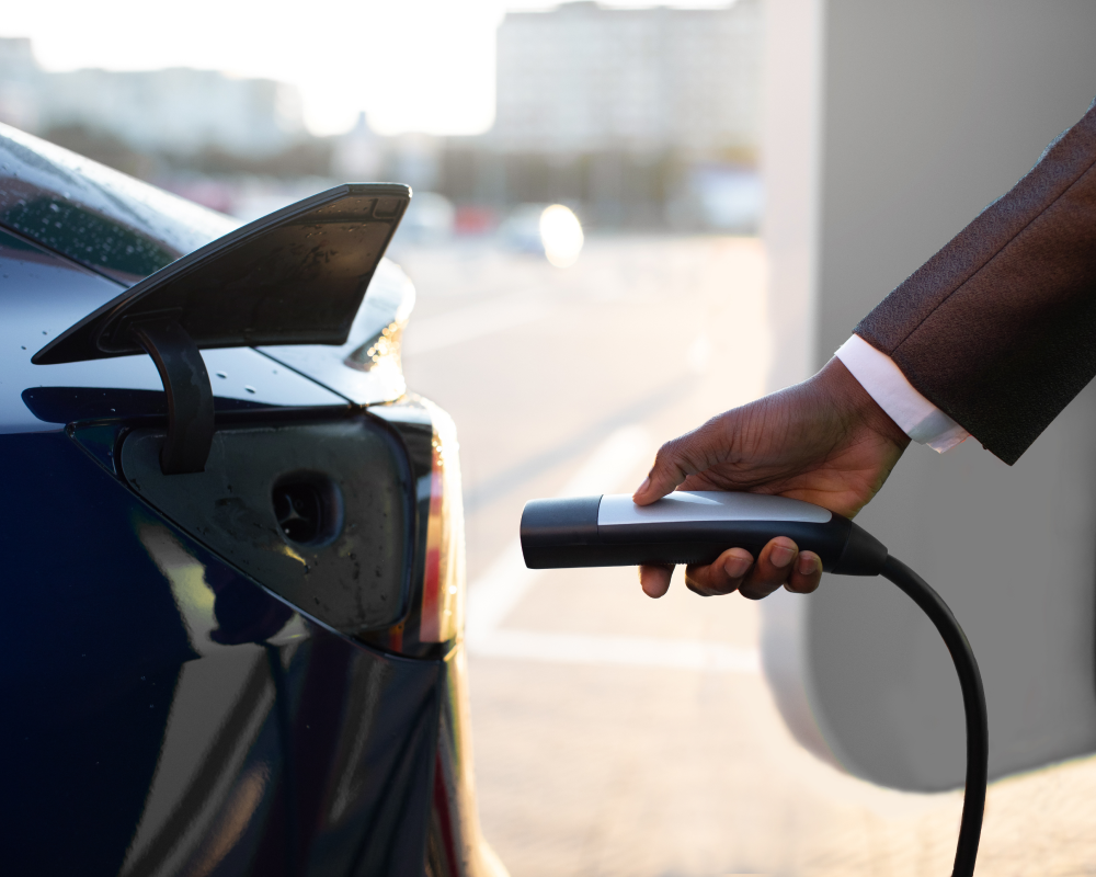 A hand plugging a NACS electric vehicle charger into their Tesla vehicle, links to LENZ EVSE product page